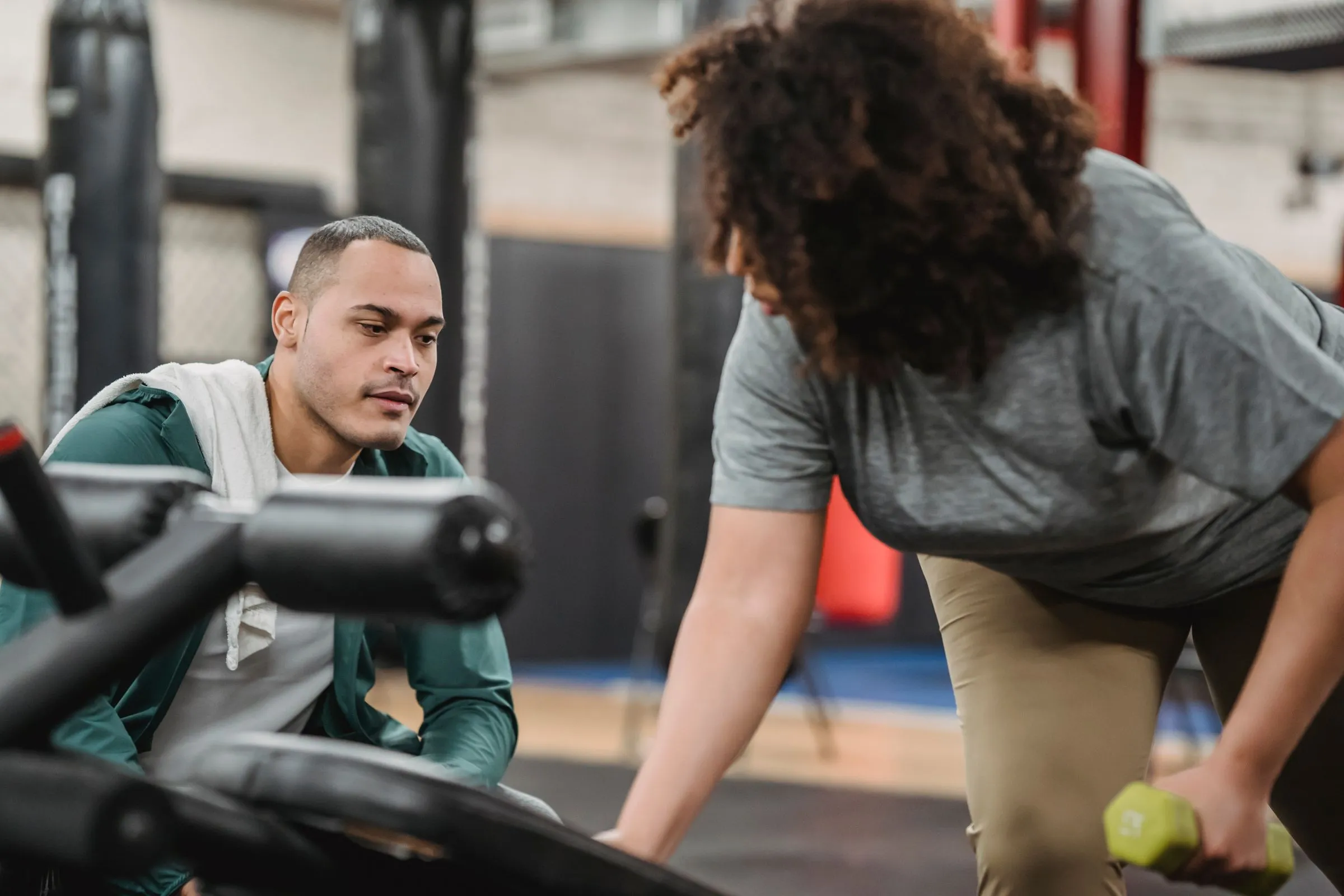 A coach standing beside a member, guiding her through a dumbbell exercise.